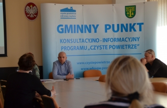 Urzednicy i mieszkany na tle napisu Gminny Punkt Konlultacyjno-informacyjny Programu Czyste Powietrze
