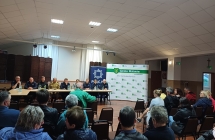 Na pierwszym planie siedzące osoby w tle grupa osób przy stole prezydialnym