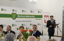 wójt przemawiający do mikrofonu na tle scianki z herbem gminy