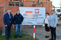 4 osoby przy tablicy informacyjnej w tle budowa budynku z cegły